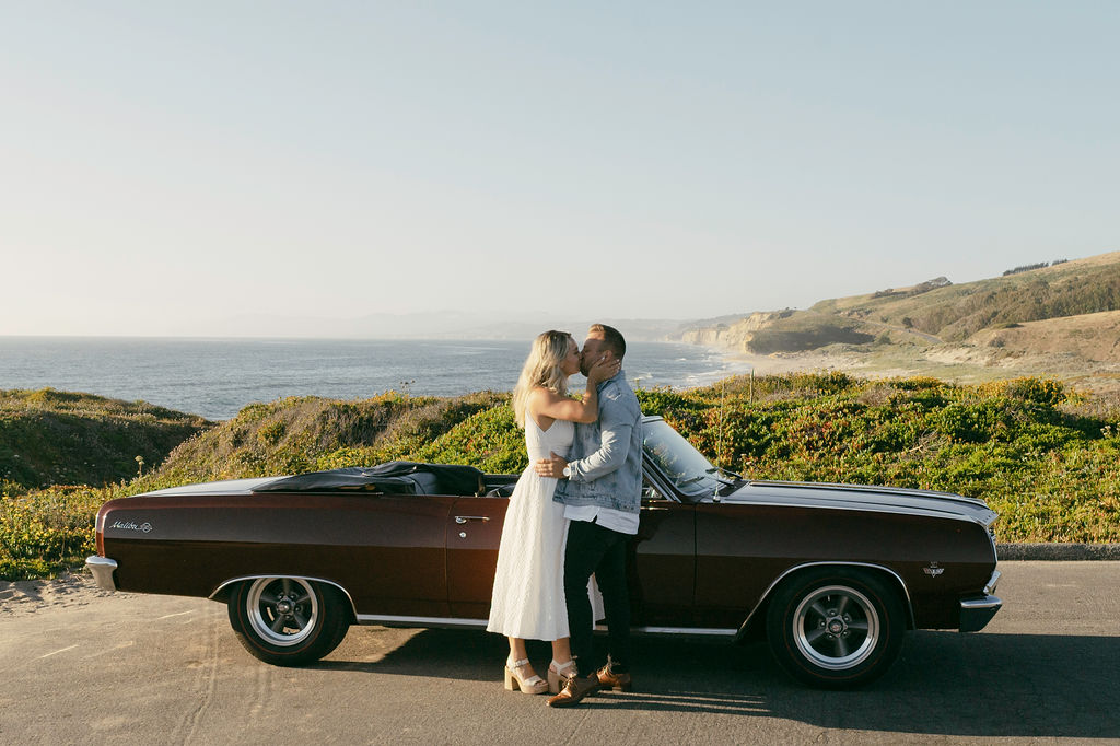 couple sitting in a car on a cliff posing at half moon bay